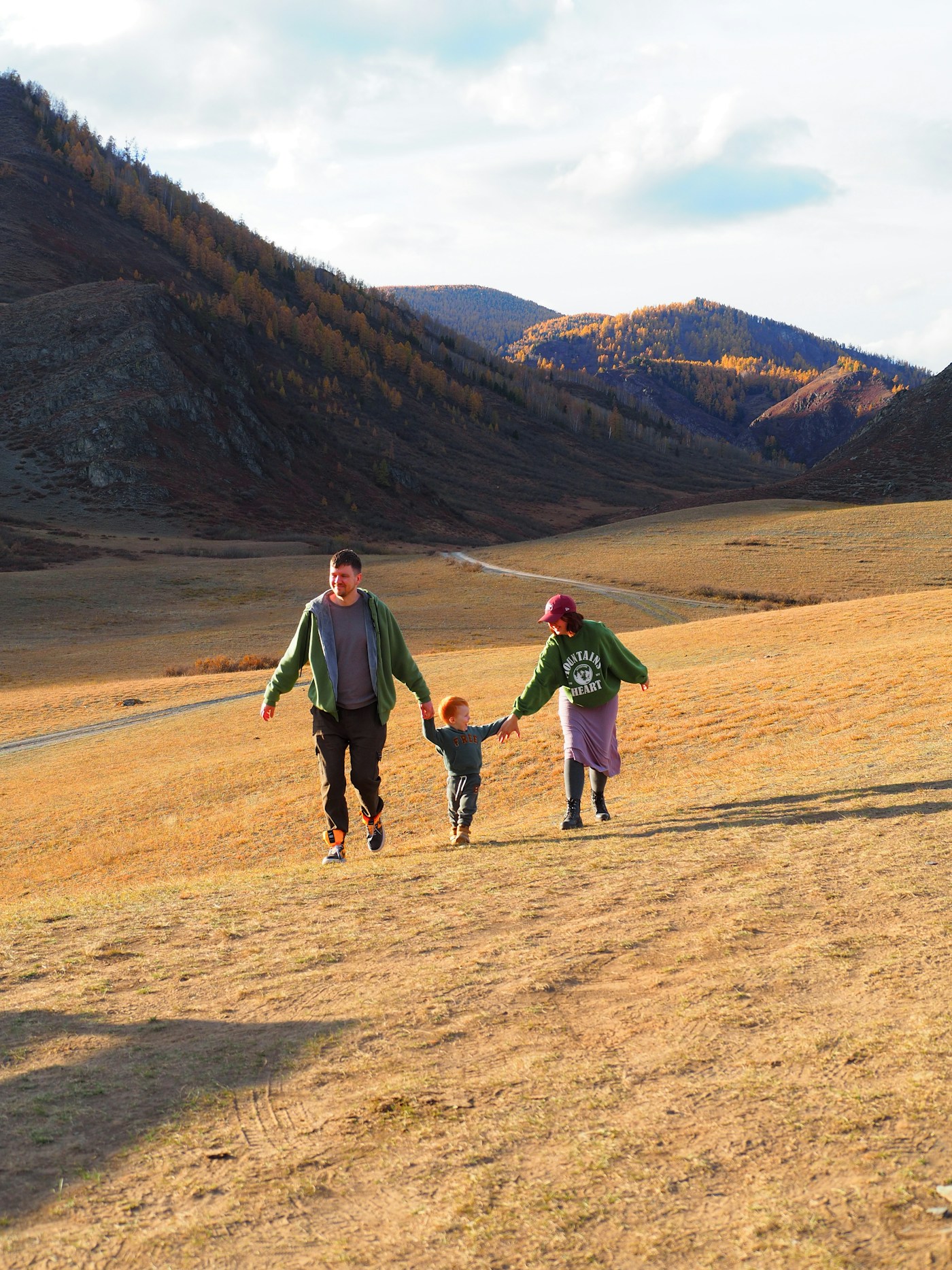 A mom, dad, and small child walk hand in hand across a dry grassy hillside