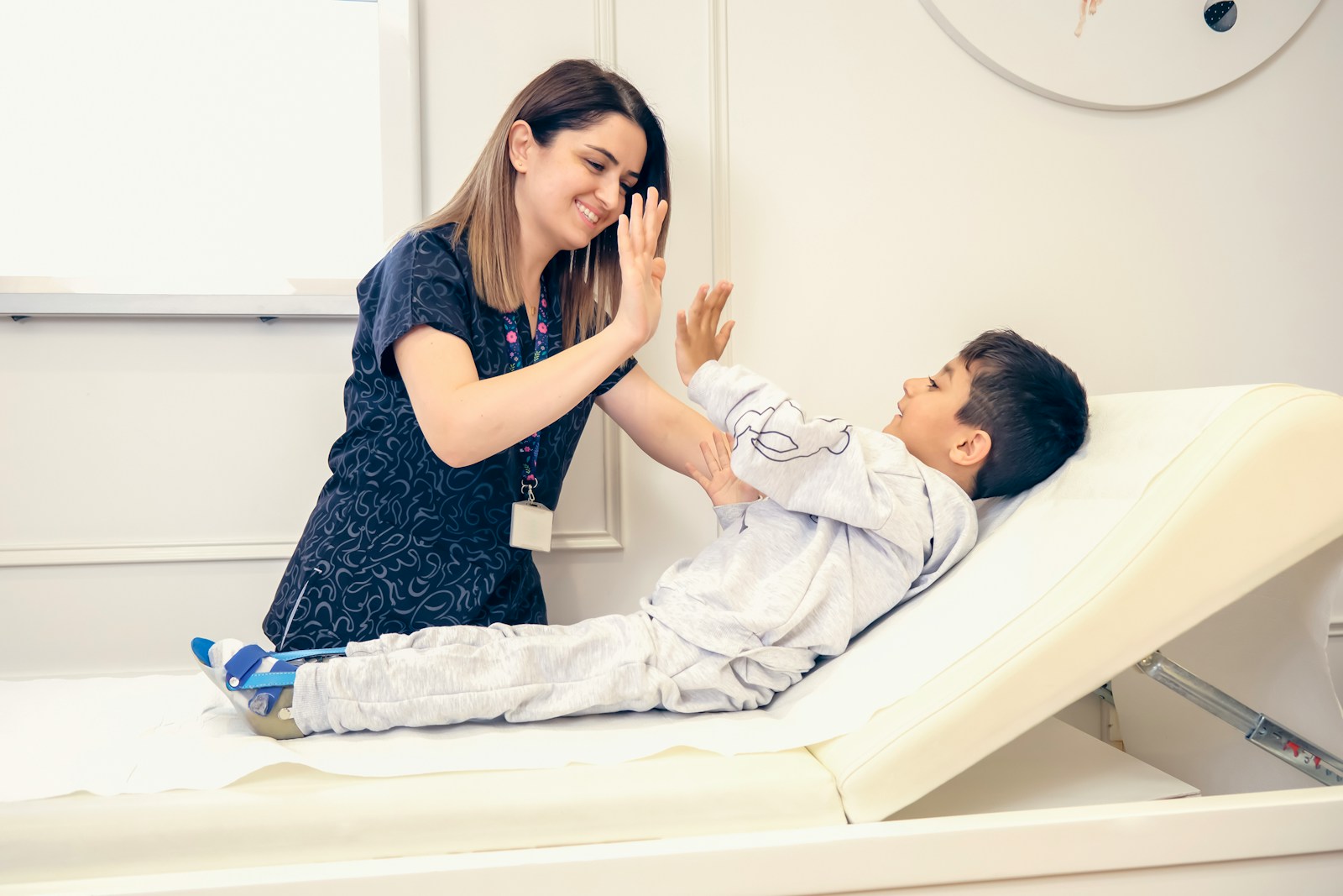 A chiropractor gives a high five to a young boy lying on the adjusting table