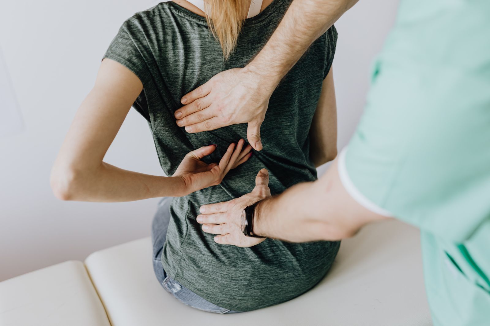 A chiropractor places both hands on a woman's mid-back during an adjustment