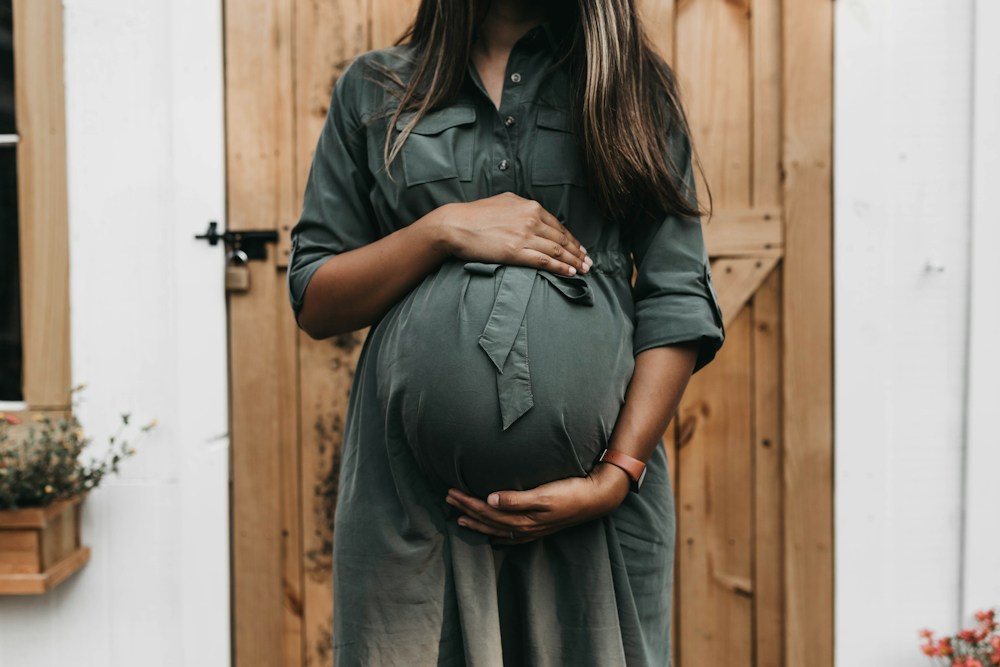 A pregnant woman holding her belly beside a wooden door
